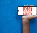 LGBT society Word on smart phone screen isolated on blue background with copy space for text. Person holding mobile on his hand and showing front of LGBT Society.(Lesbi, Gay, Bisexual, Transgender).
